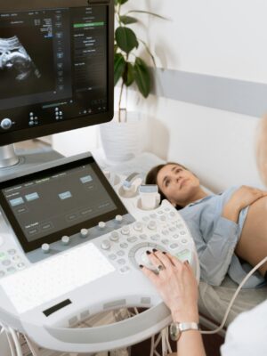 Pregnant woman undergoes ultrasound scan by medical professional in hospital room.